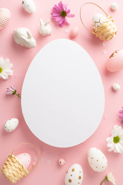 istock Classy Easter motif picture. Vertical top view shot of eggs, lively chrysanthemums, ceramic bunnies on a light pink base, with open egg-shaped spot for messages or marketing 2060685609