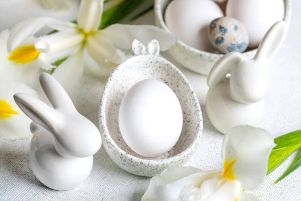 istock Closeup one white egg in marble bowl with bunny ears, small bunnies, Iris flowers around it on white 2060691456
