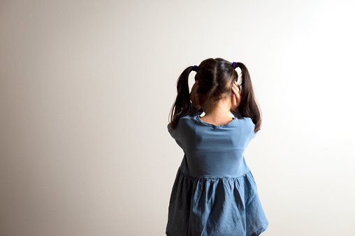 Back view of little caucasian girl with double ponytail who is covering her ears to not hear anything. Representing family pressure and strict education.
