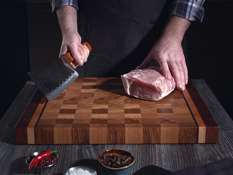 A man is about to cut a large piece of pork meat with a large knife. In the home kitchen. Homemade food cooking concepts.
