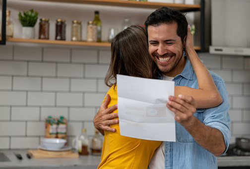 Happy Latin American couple at home reading good news in a letter they got in the mail - lifestyle concepts