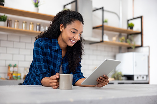 Happy African American woman drinking coffee at home while watching videos on a digital tablet â lifestyle concepts