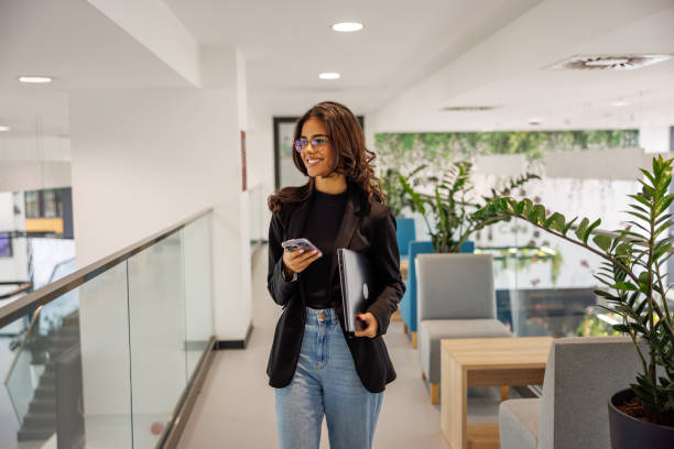 istock Smiling young woman messaging while walking in business building 2060746898