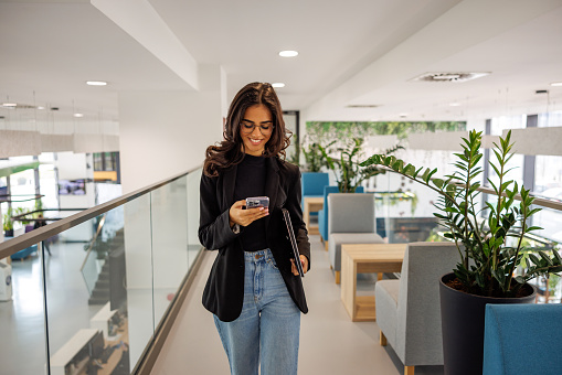 Smiling young woman messaging while walking in business building