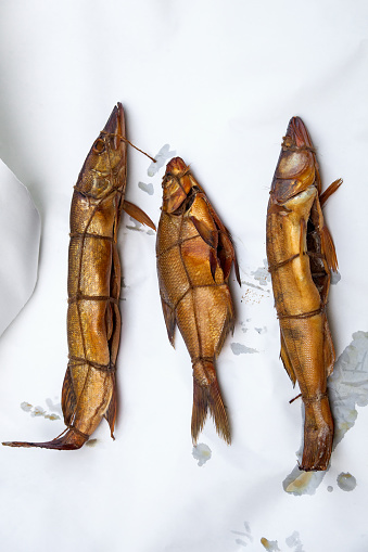 Assort of different kind of freshwater fish zander, pike and common bream smoked in smokehouse. Beautiful delicious dried smoked fish with spices for home use on white paper.