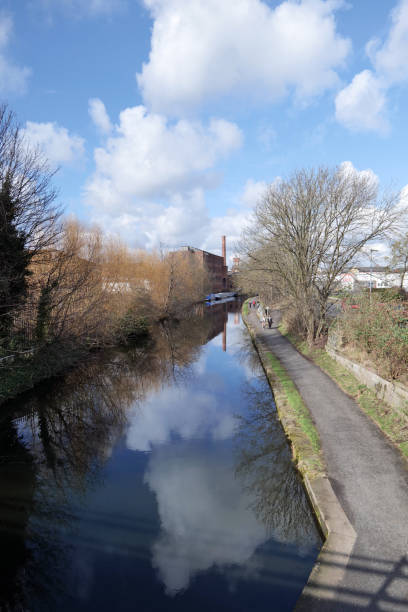 Leeds, UK 03 03 2025 Looking North West along the Leeds Liverpool canal, with people out enjoying walking along the toe path. A tradional mill chimney can be seen reflectied in the calm canal  water.