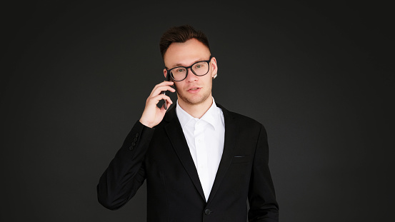 Business call. Mobile management. Corporate communication. Confident serious man in suit talking on phone discussing work isolated on dark black empty space background.