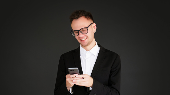 Mobile chat. Gadget people. Internet communication. Happy cheerful business man texting message using phone isolated on dark black empty space background.
