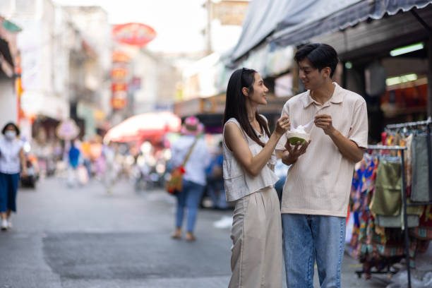 アジア人観光客の友人が小売市場の通りを歩いていて、屋台の食べ物でおいしいアイスクリームを買っています。 - women eating ice cream indigenous culture ストックフォトと画像