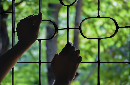 Hands of teenager boy on the metal fence window at the detention center because he was detained for inappropriate behavior, soft focus, freedom and detention concept.