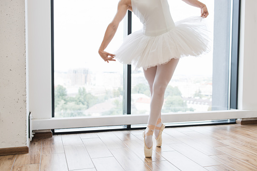 Cropped view of lags of beautiful graceful ballerina in white swan dress. Young ballet dancer practicing before performance in black tutu, classical dance studio, copy space.