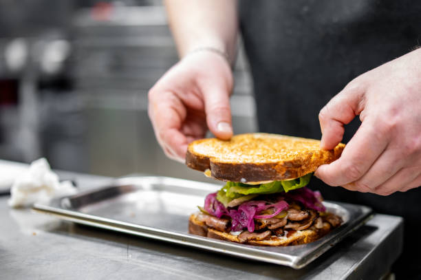 istock A chef assembles a gourmet sandwich with fresh vegetables and grilled meat on toasted bread in a professional kitchen 2060781744