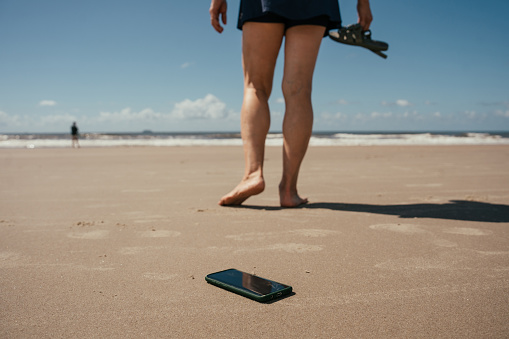 Woman walking along the beach and heating cell phone on the floor