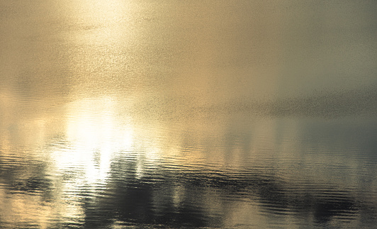 Full frame of brilliant gold textured ripples on ocean surface reflecting the sunrise, shot at sunrise while swilling in the ocean of Western Australia.