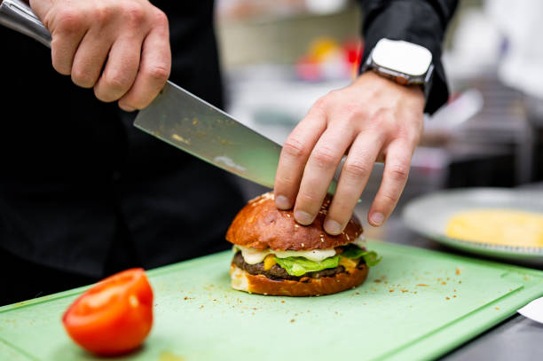 istock A chef deftly slices a freshly made burger with precision on a green cutting board. Tomato slices await nearby 2060824205