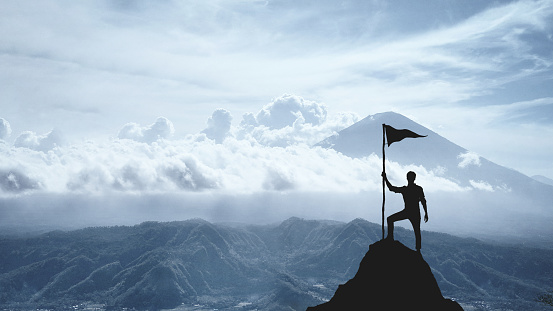 Silhouette of a man on the peak of a mountain, concept of victory and achievement.