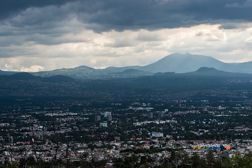 Brooding skies over sprawling Mexico City cityscape, with the silent sentinels of mountains standing guard.