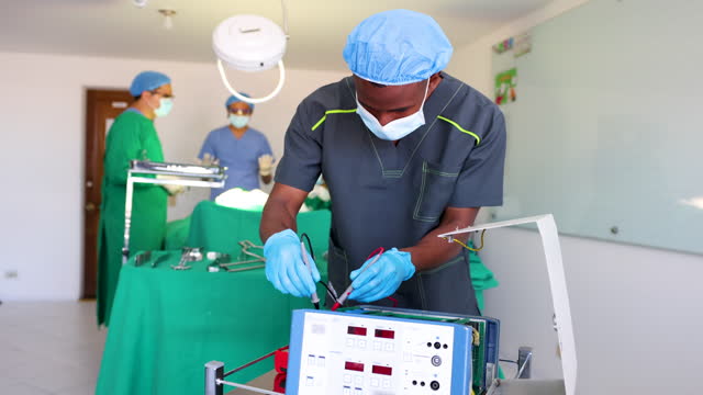 Male technician correcting a machine while surgeons and surgical instrument technicians wait to start the surgery