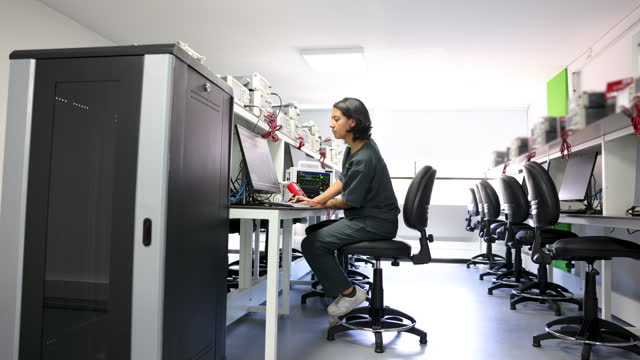 Female technician working at a hospital checking medical equipment using a computer and multimeter