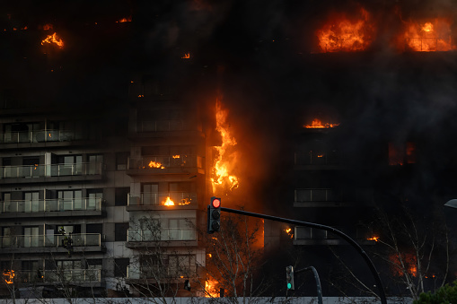 Large fire in a residential building in the city of Valencia, Spain, burning rapidly with firefighters on the second floor trying to escape the flames.