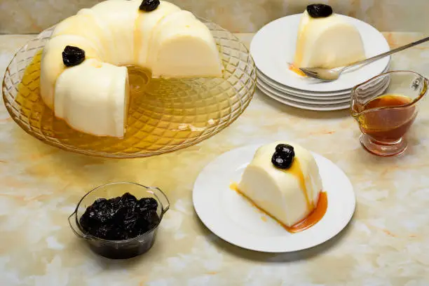 Blancmange decorated with plums, a slice on a white plate, yellow marble bottom