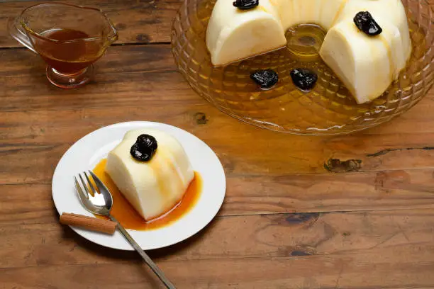 Blancmange decorated with plums, one slice on a white plate, on a wooden board