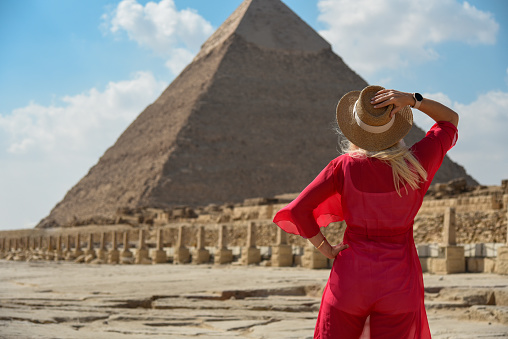A girl in a red dress looks at an Egyptian pyramid.