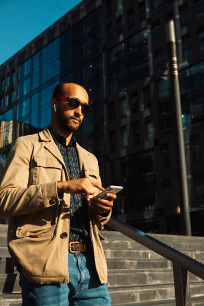 istock Young Afro man wearing sunglasses using smartphone to text message near modern business centre outdoor. 2060904247