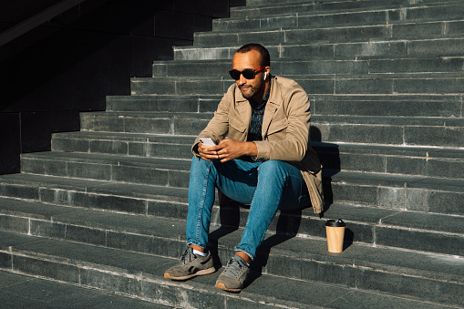 Portrait of young handsome african american man sitting on steps using mobile