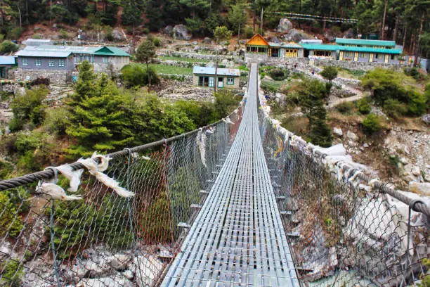 Trekkers on the Everest Base Camp trek pass over steel rope bridges over streams adorned with prayer flags near Lukla,Nepal