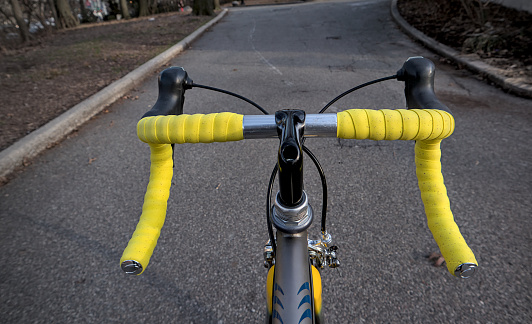 bike handlebar detail with bright yellow bar tape (bicycle cockpit, cycling) integrated shifters, brifters, black quill threaded stem, headset, titanium frame, silver aluminum bars, exposed cables