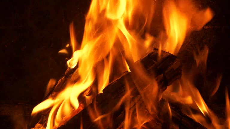 Firewood burning in a fireplace, with vibrant flames and embers, close-up view