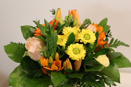 Colorful bouquet of spring flowers - yellow daisies, orange lilies and light pink roses with some green leaves. Celebrate special events and decorate home with these. Closeup color image.