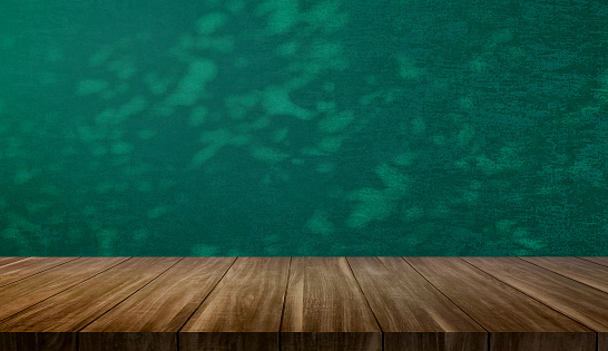 empty wood table at foreground with dark green color fabric wallpaper at background with branch and leaves shadow for product placement displayed. background for natural concept.