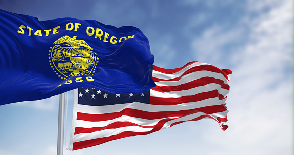 Oregon state flag waving with the american flag on a clear day. The Oregon flag is two-sided with navy blue and gold colors. Selective focus. Fluttering fabric. Waving flag