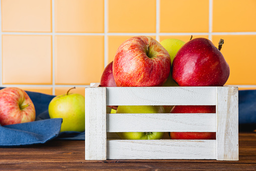 Red and yellow apples in a crate on a wooden table. Side view of fresh fruits.