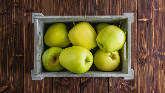 Yellow apples in a crate on a wooden background. Top view of fresh fruits.