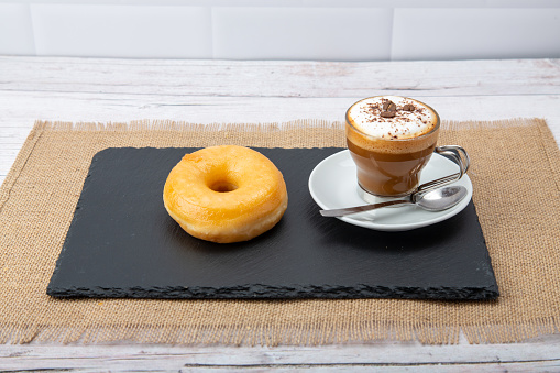 Steaming cup of coffee cozies up to a plate of freshly glazed donuts