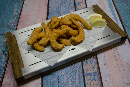 Seafood. Top view of fried shrimps with lemon in a metal board on the wooden table.