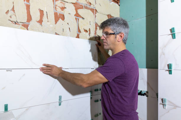 istock Tiler with protective glasses placing a piece of large format tile on a brick wall in a bathroom renovation 2061103095