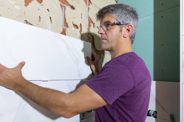 istock Side portrait of a tiler wearing protective glasses placing a large format tile piece on a brick wall in a bathroom renovation. Home renovation concept 2061103164
