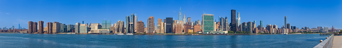 High Resolution Stitched Panorama of New York Skyline with UN Building (Headquarters of the United Nations), Chrysler Building, Empire State Building, World Trade Center Tower, Manhattan Upper East Side Residential and Office High-rises, FDR drive, Queensboro Bridge, water of East River, Green Trees and Morning Blue Sky with Clouds. Canon EOS 6D (Full Frame censor) DSLR and Canon EF 85mm f/1.8 lens. 7:1 Image Aspect Ratio. This image is downsized to 50MP. The Original image resolution is 190MP or 36,467 x 5,210 px.