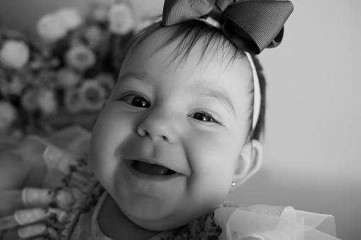 Portrait of daddy with an baby girl with bow isolated in wall background. Cute baby in dads arms closeup. Dad holds in hands 6 month old little girl. Father hugging his daughter. Black and white photo