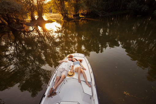 High angle view of beauitful young couple in love enjoying summer vacation, lying down and relaxing while sailing to the sunset on a boat