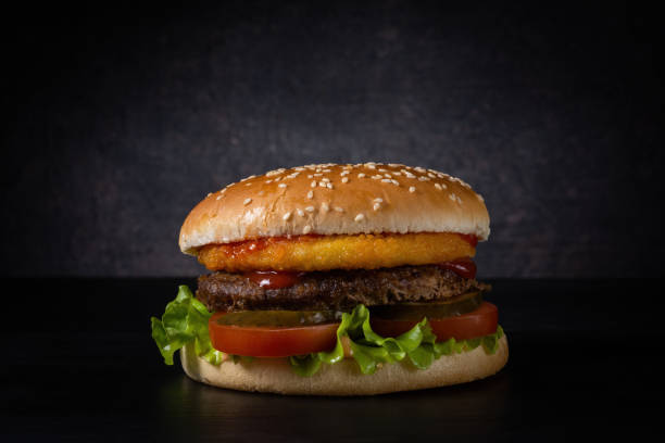 fresh burger with sesame bun, beef patty and vegetables on a dark background with a gradient spot of light. moody photo with copy space. side view fresh burger with sesame bun, beef patty and vegetables on a dark background with a gradient spot of light. moody artistic photo with copy space. side view brat burger stock pictures, royalty-free photos & images