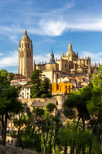 Segovia Cathedral medieval Gothic building with richly decorated spires, among green trees, summer, Spain.