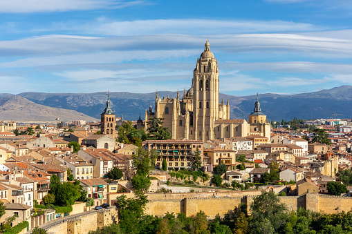 Segovia, Spain skyline with Segovia Cathedral at the top, churches, medieval architecture, residential buildings city walls and mountains in the background.