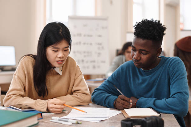 Two Students Studying at Table in Library Front view portrait of two multiethnic students Asian woman and Black man studying together sitting at table in college library male chinese student stock pictures, royalty-free photos & images