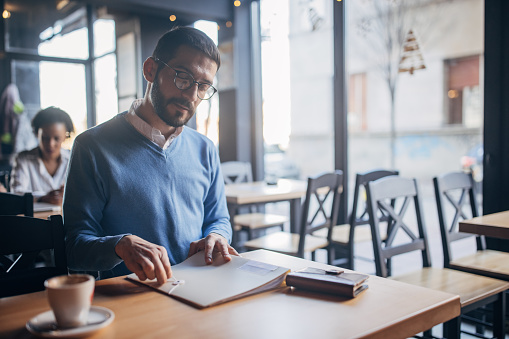 Charming businessman looking at file folder, he is sitting in cafe.