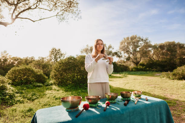 mulher jovem bonita em pé com címbalos na frente de cinco tigelas de canto tibetano em seu jardim - spirituality hand on heart meditating women - fotografias e filmes do acervo